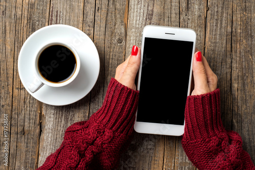 Woman using a smartphone in warm sweater over wooden background photo