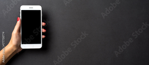 Female hand holding white mobile phone against dark elegant background photo