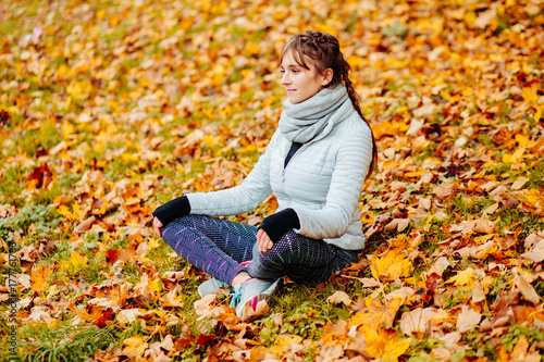 Woman sitting on bright yellow autumnal leaves enjoying beautiful autumn weather in park on forest. Many yellow golden leafs