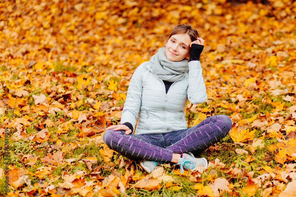 Woman sitting on bright yellow autumnal leaves enjoying beautiful autumn weather in park on forest. Many yellow golden leafs