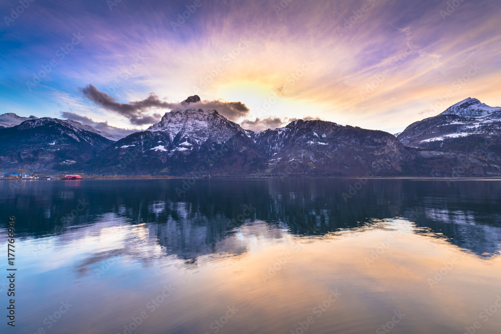 Bright sunset colors. Swiss Alps. Colorful sunset over the mountains and lake. Tops in the snow reflected in lake water.
