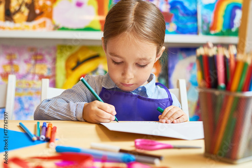 Portrait of adorable little girl drawing pictures during art and craft class in pre-school
