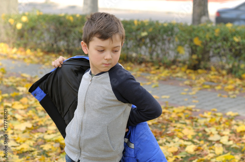 Boy puts on a blue jacket walking in the autumn park