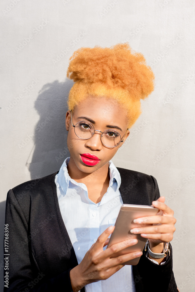 Fototapeta premium Lifestyle portrait of an african businesswoman in casual suit using smart phone on the gray wall background