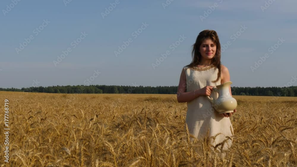 Woman in linen dress with a jug at goldish wheatfield Woman in linen dress with a jug at goldish wheatfield