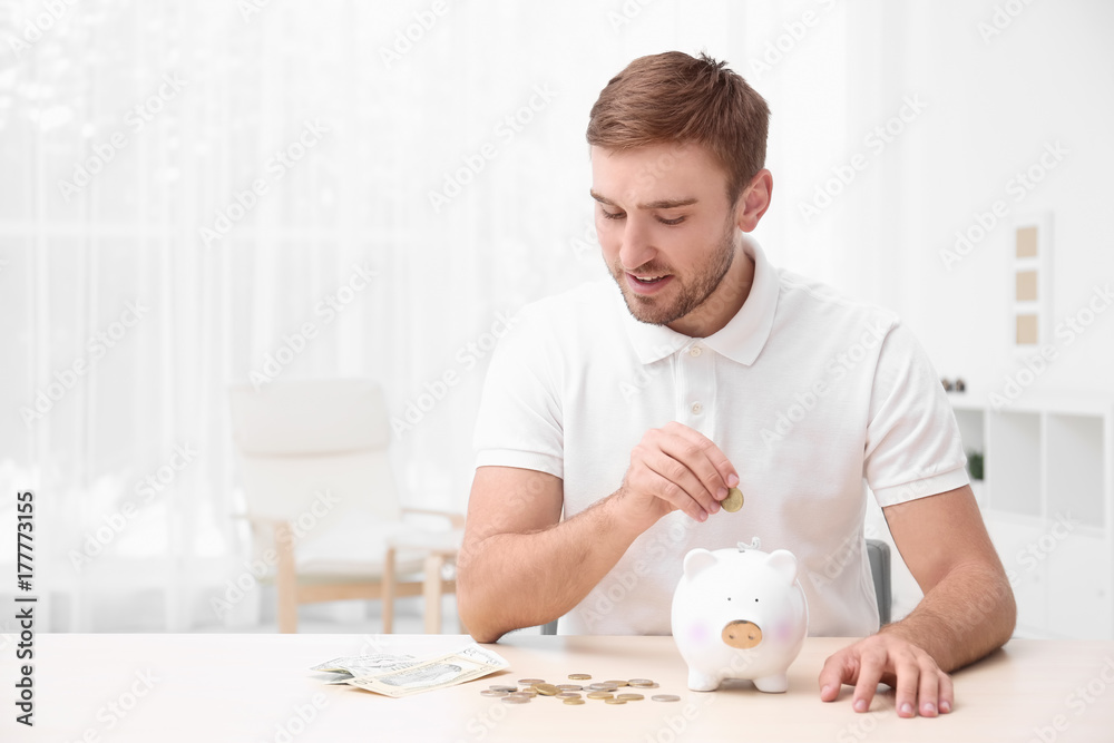 Young man with piggy bank at table Young man with piggy bank at table