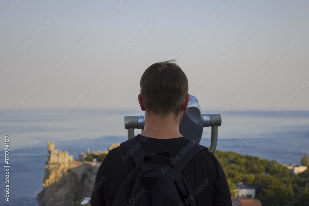 Obraz premium man in a black T-shirt looking through binoculars at sea