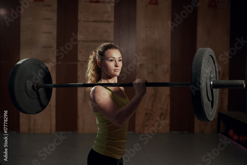 strong woman holds a barbell on her shoulder in the gym
