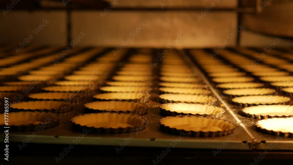 Industrial process of Empty Pies base pastries made from biscuits and butter in the hot oven on a conveyor belt in a bakery factory Industrial process of Empty Pies base pastries made from biscuits and butter in the hot oven on a conveyor belt in a bakery factory