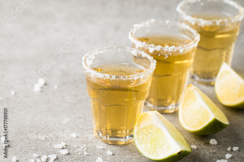 Macro focus photo of shots of golden Mexican tequila with lime and salt on wooden background. Alcoholic drink concept.