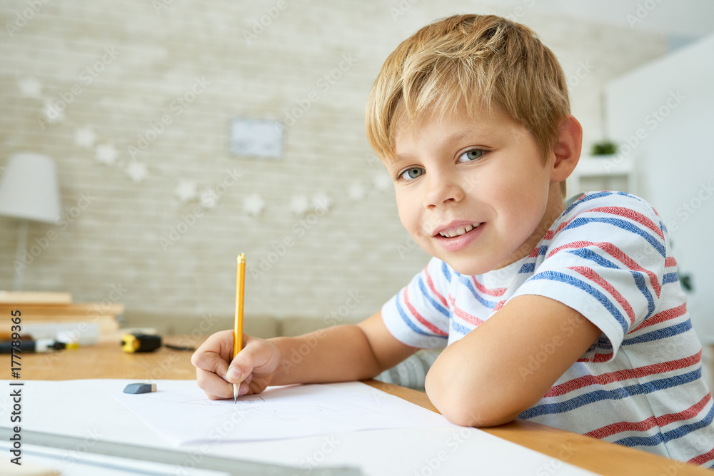 Portrait of cute little boy looking at camera and smiling while sitting at desk doing homework, copy space Portrait of cute little boy looking at camera and smiling while sitting at desk doing homework, copy space