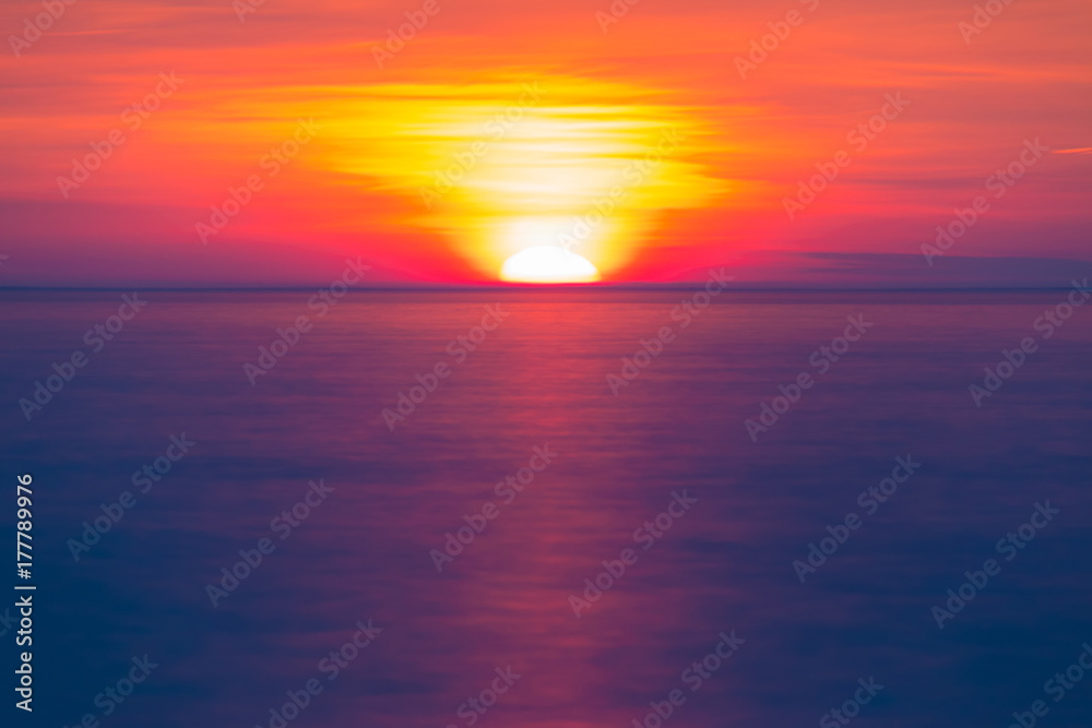 Long exposure view of the half of setting sun over the sea horizon