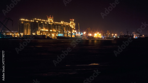Panorama image of the illuminated cargo port at night, cargo ships and cranes © alexxndr