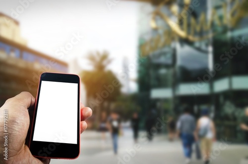 hand using blank screen mobile smart phone with department store shopping mall blurred background, internet, searching information, social media, payment and shopping online concept