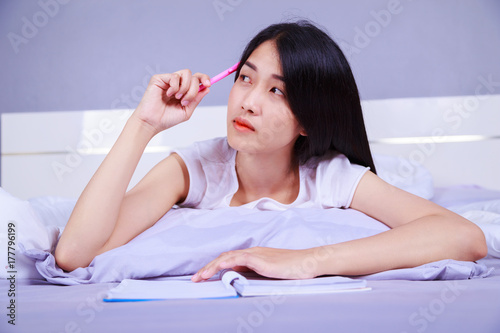 woman thinking and writing a book on her bed in bedroom