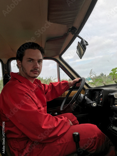 Young car mechanic in red suit driving an old yellow car