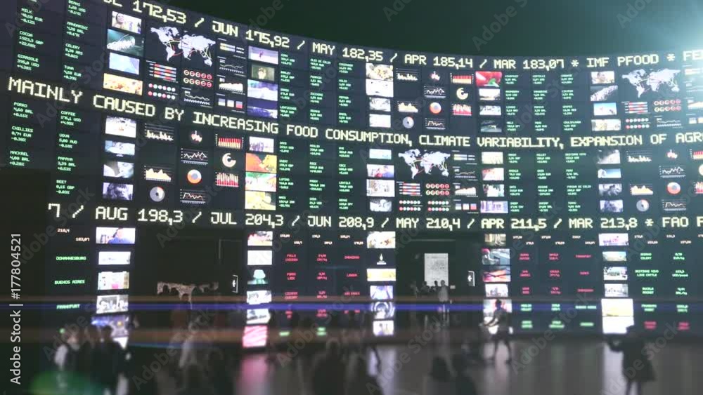 Wall Screen display financial information, people walking near the screens.