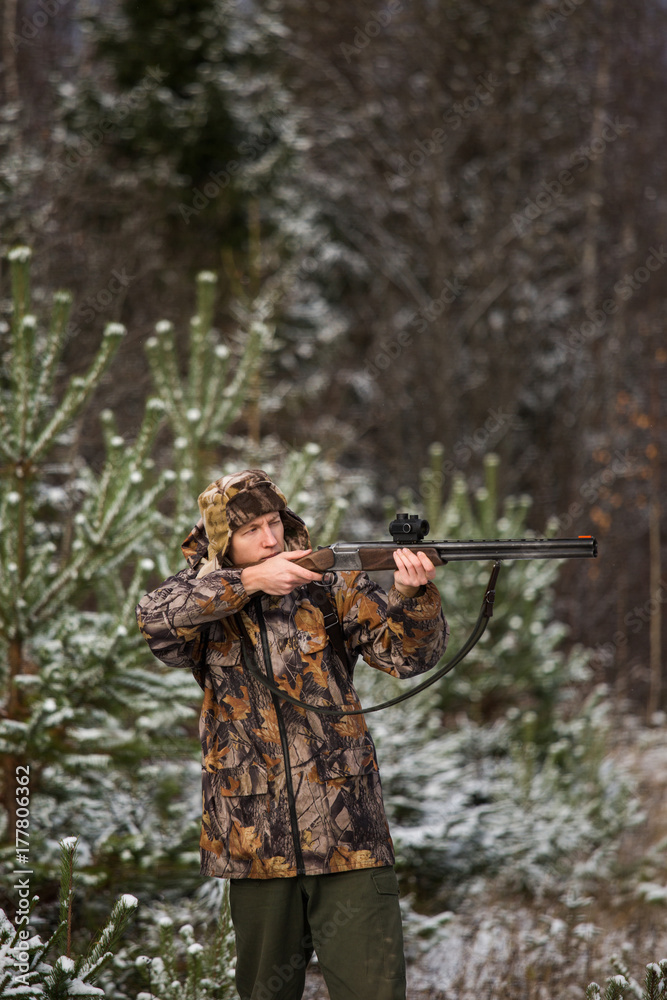 Male hunter in camouflage and with backpack, armed with a rifle, standing in a snowy winter forest. Male hunter in camouflage and with backpack, armed with a rifle, standing in a snowy winter forest.