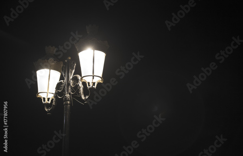 on the left there is a forged street lamp with two lamps  on the background of the night photo