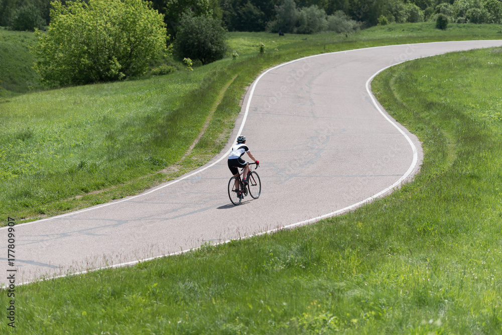 Obraz premium Sport. Cyclist riding a bike on an open road. Green field and trees as a background