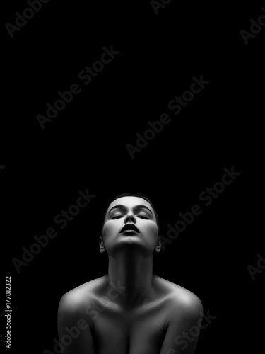 beautiful young naked woman posing sensually holding head up on black background with copy space, monochrome