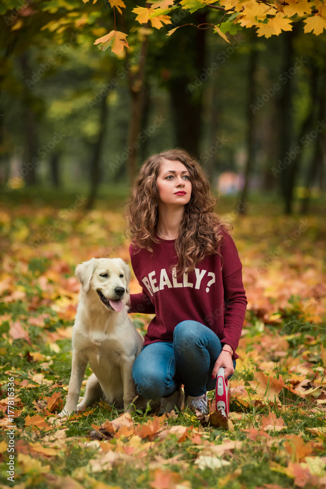 Portrait of a curly young woman hugging her golden retriever dog in the autumn park. yellow leaves background