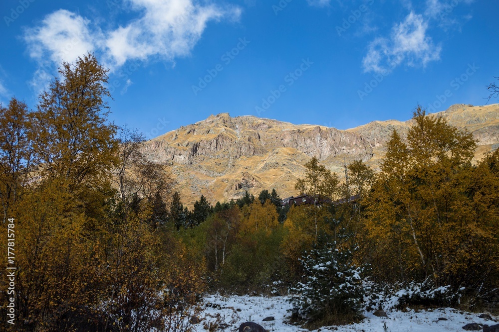 Осенний лес в горном ущелье, облачное небо над вершинами. Дикая природа Северного Кавказа, живописный пейзаж