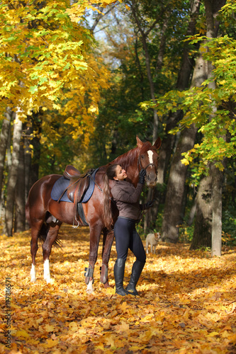 Equestrian girl walks bay arabian horse in autumn woods