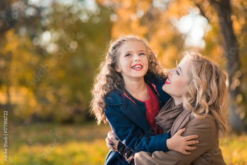 Mother with daughter having fun at autumn time. Woman and young girl playing in the park smiling, hugging. happy family concept.
