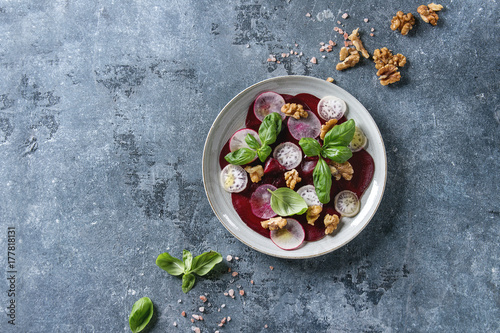 Tableau sur toile Vegan beetroot carpaccio salad with radish, basil, olive oil and walnuts in ceramic plate over blue texture background