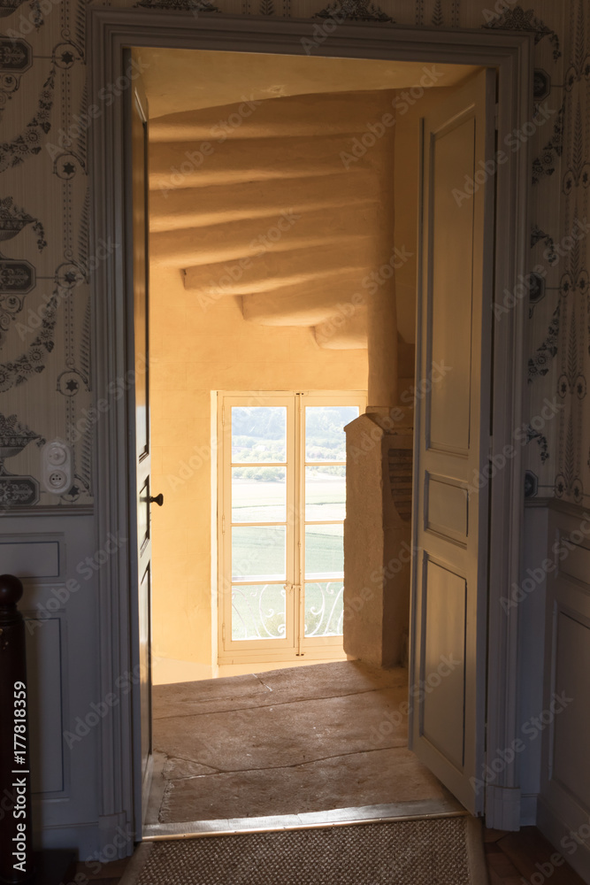 Through a doorway we look into a staircase with a window where a warm sunlight falls inward, the yellowish colors enhance the warmth in the picture.