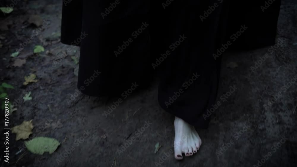 close up shot of the pale feet of a woman who walks barefoot along the gray park road, a woman dressed in a long dress