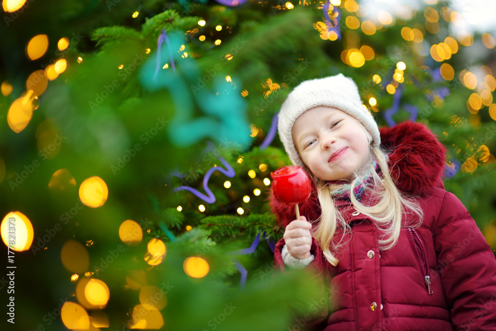 Adorable little girl eating red apple covered with sugar icing on traditional Christmas market. Adorable little girl eating red apple covered with sugar icing on traditional Christmas market.