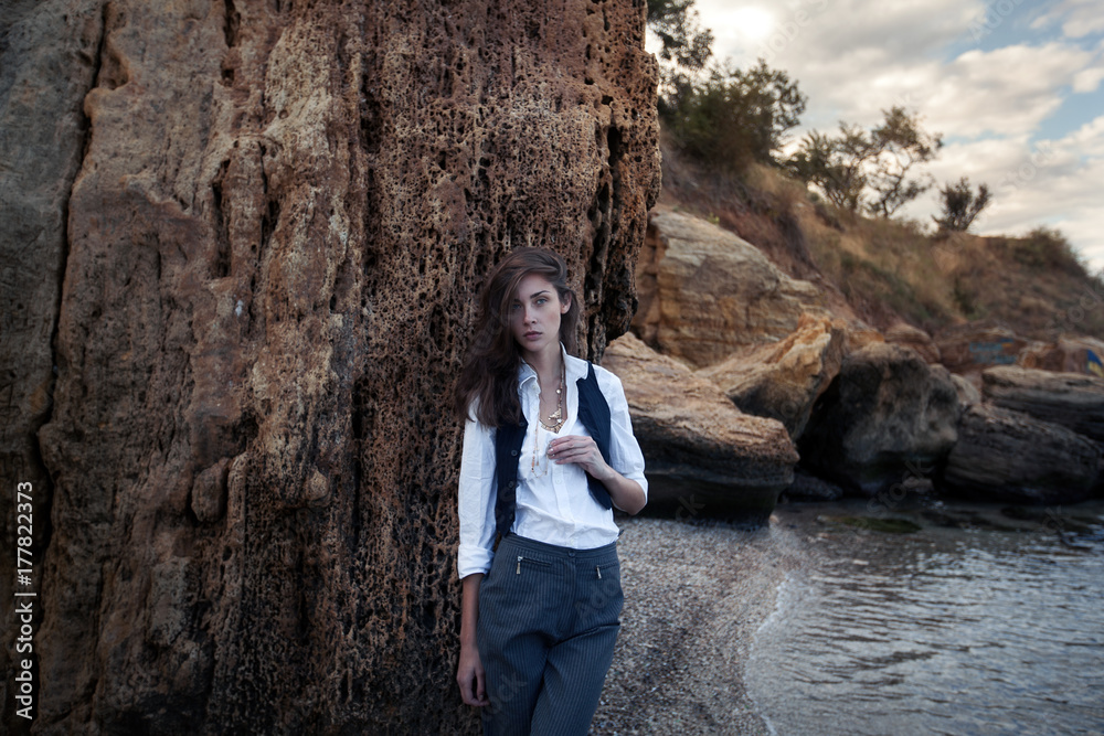 business woman on suit vest and white shirt standing near big stone on the sea cost