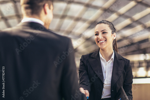 Two smiling young business people shaking hands while standing outdoors photo