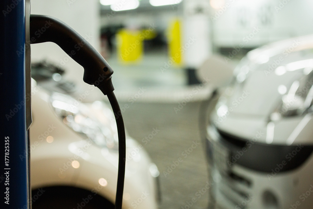 Electric car charged on a charging station in a indoor parking of shopping center by night. 