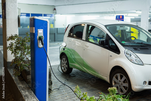 Electric car charged on a charging station in a indoor parking of shopping center by night. 