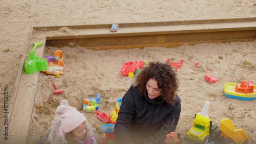 Mother playing with her daughter in a sandbox photo