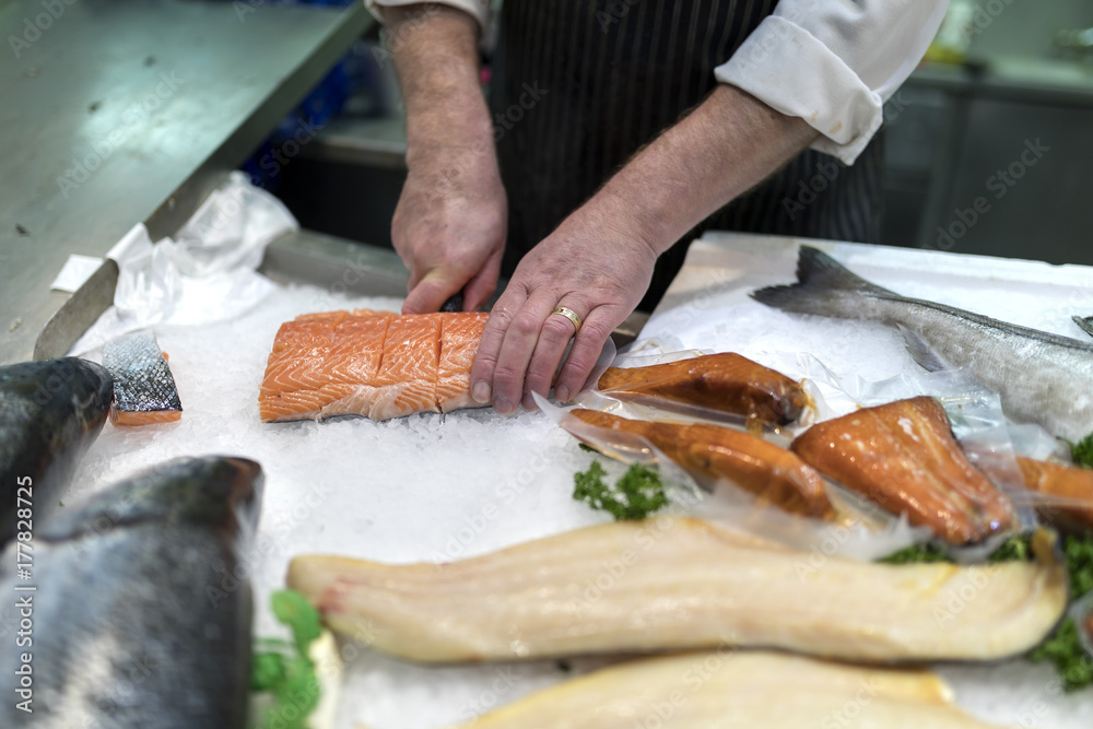 British fish monger slicing, filleting or cutting fresh slamon on ice on a market staff in Yorkshire, England in the UK