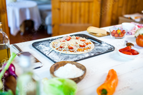 raw fresh homemade traditional italian pizza with tomatoes, cheese and han on wooden cooking table with ingredients. wallpaper for pizzeria and food concept