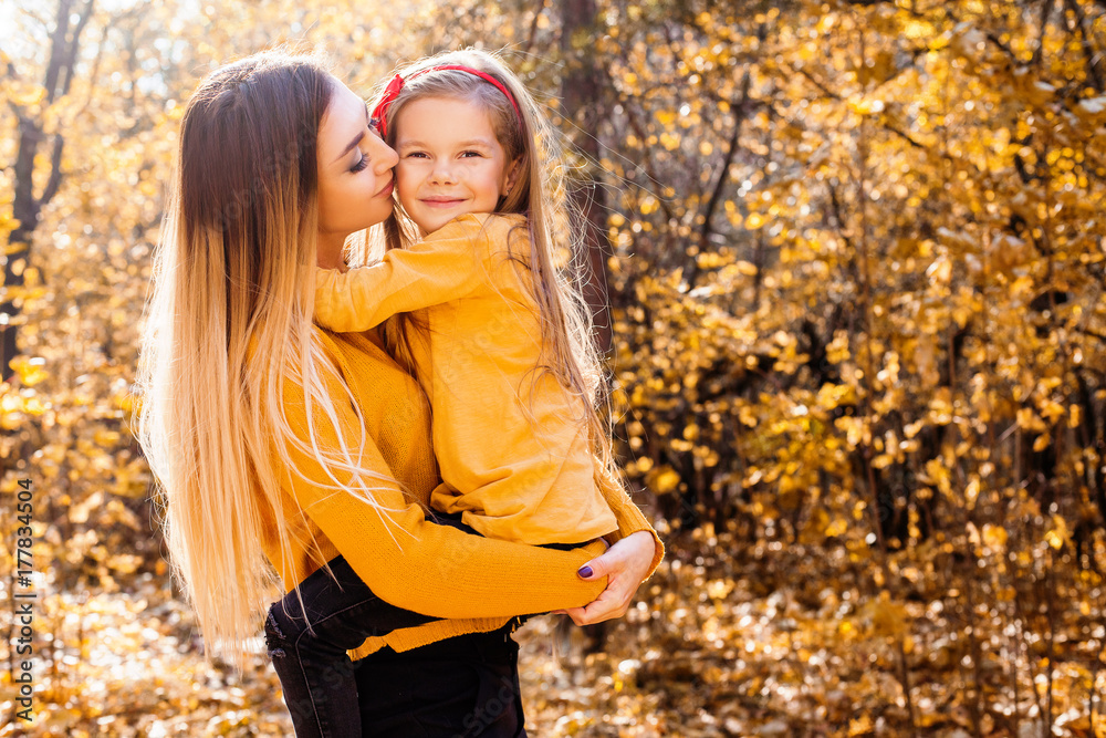 Happy smiling mother and daughter in yellow pullovers in the autumn park. Happy family outdoors. Autumn park. Leaf fall. Happy smiling mother and daughter in yellow pullovers in the autumn park. Happy family outdoors. Autumn park. Leaf fall.