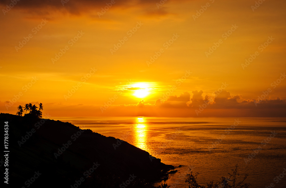 Silhouettes of palm trees, bright yellow clouds, romantic beach on a tropical island during sunset.