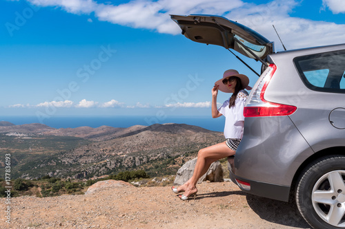 Woman traveler sitting on hatchback car with mountain background