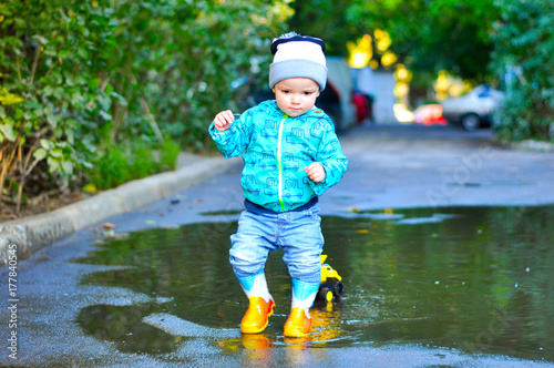 The little boy in colored rubber boots playing with his yellow toy truck in puddles 