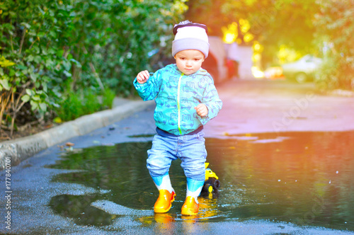 The little boy in colored rubber boots playing with his yellow toy truck in puddles 