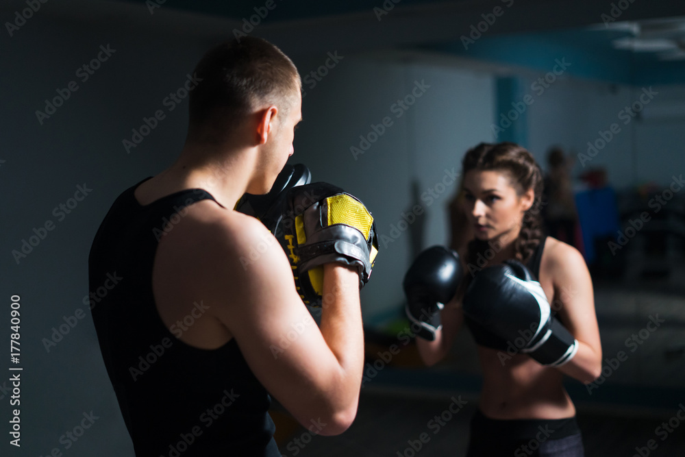 Young fighter boxer fit girl wearing boxing gloves in training  with  personal trainer in gym. Low key image. Moment before punch