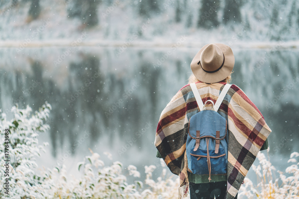 Young traveling girl standing in front of beautiful mountain lake. Winter is coming, first snowfall. Wanderlust and boho style Young traveling girl standing in front of beautiful mountain lake. Winter is coming, first snowfall. Wanderlust and boho style