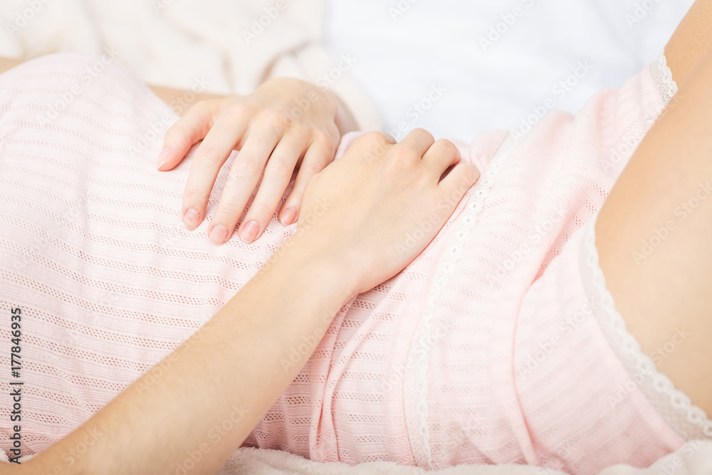 Young woman suffering from abdominal pain while sitting on bed at home. Stomach pain. In stress. Young woman suffering from abdominal pain while sitting on bed at home. Stomach pain. In stress.