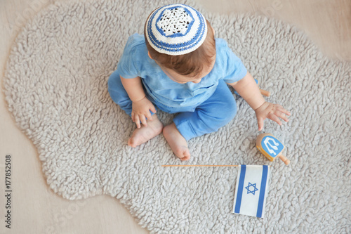 Cute baby in kippah playing with dreidels while sitting on floor