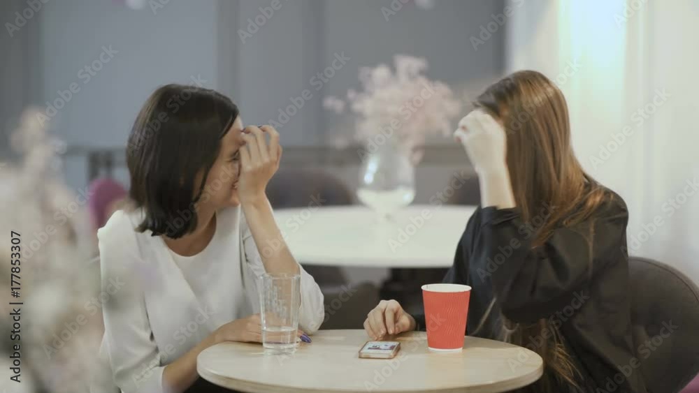 Two young girls whisper the secrets in ears in cafe Two young girls whisper the secrets in ears in cafe